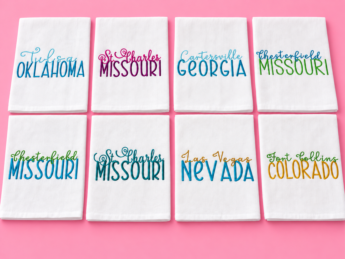 Colorful city and state embroidered tea towels on a pink background