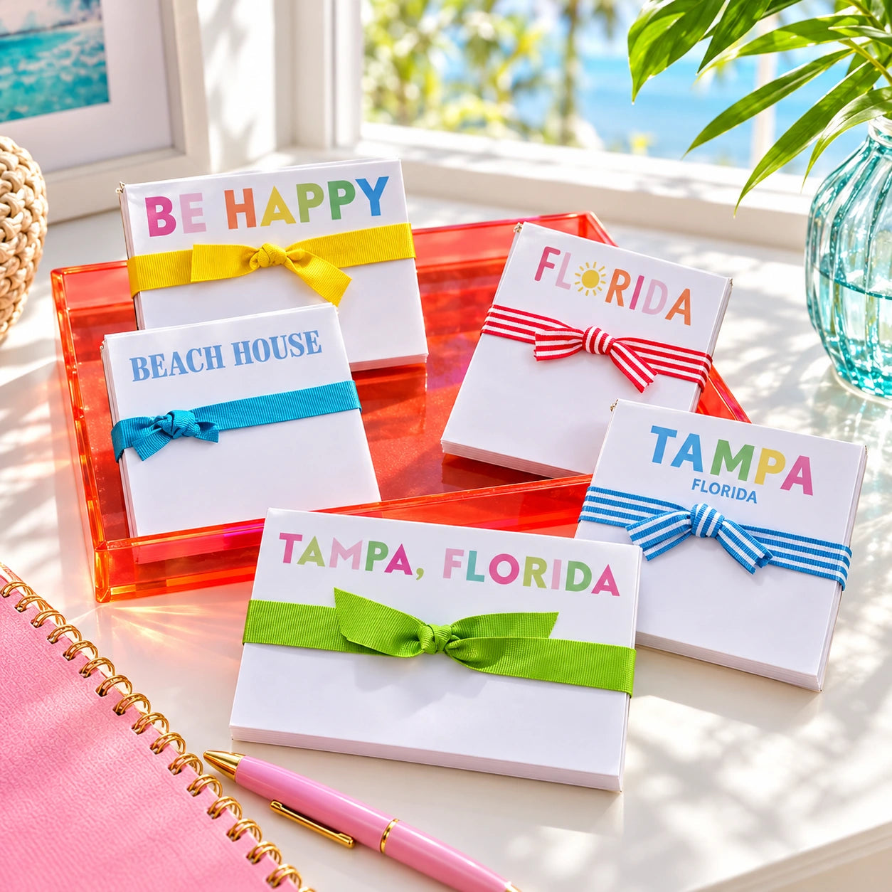 Colorful ribbon-wrapped notepads styled on a sunny coastal desk